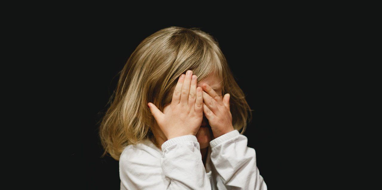 niña con las manos en la cara en fondo negro