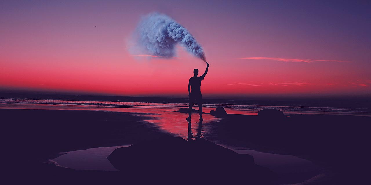 hombre sosteniendo un bote de humo en la orilla del mar