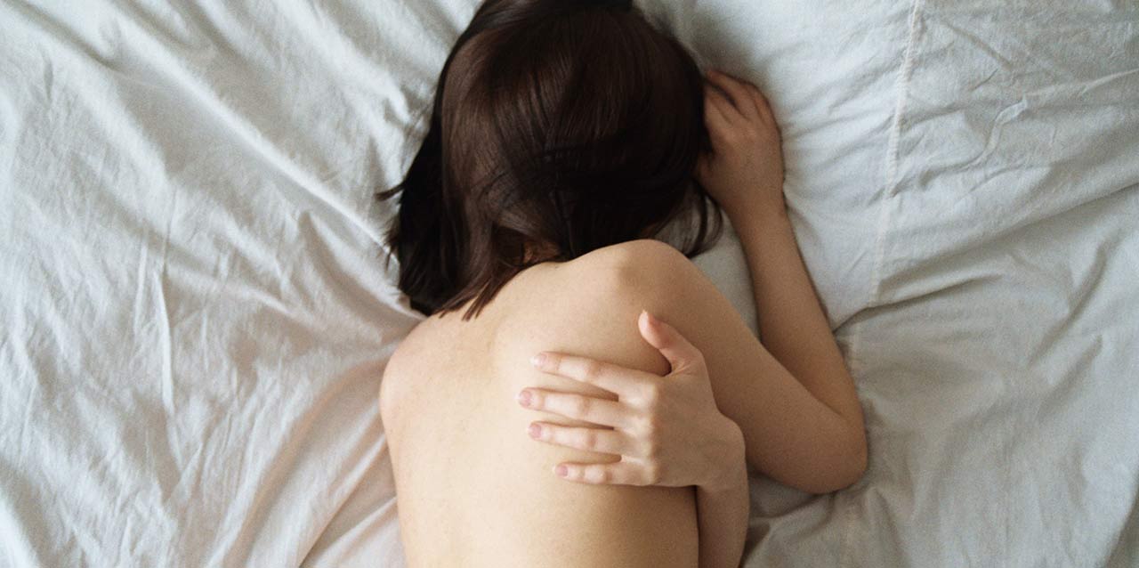 mujer tumbada en cama abrazándose mujer tumbada en cama abrazándose
