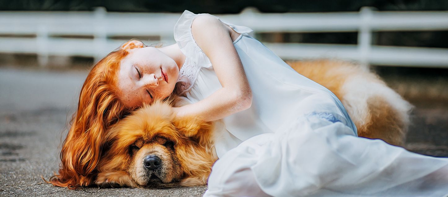 una niña pequeña de pelo pelirrojo largo dormida sobre su perro chow chow