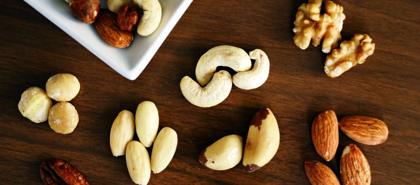 distintos frutos secos dispuestos sobre una mesa de madera como avellanas, almendras, nueces, anacardos