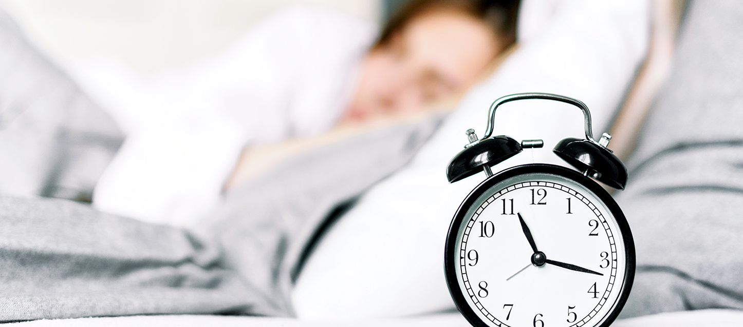 reloj despertador antiguo de color blanco y negro en la mesita de noche y una chica durmiendo detrás