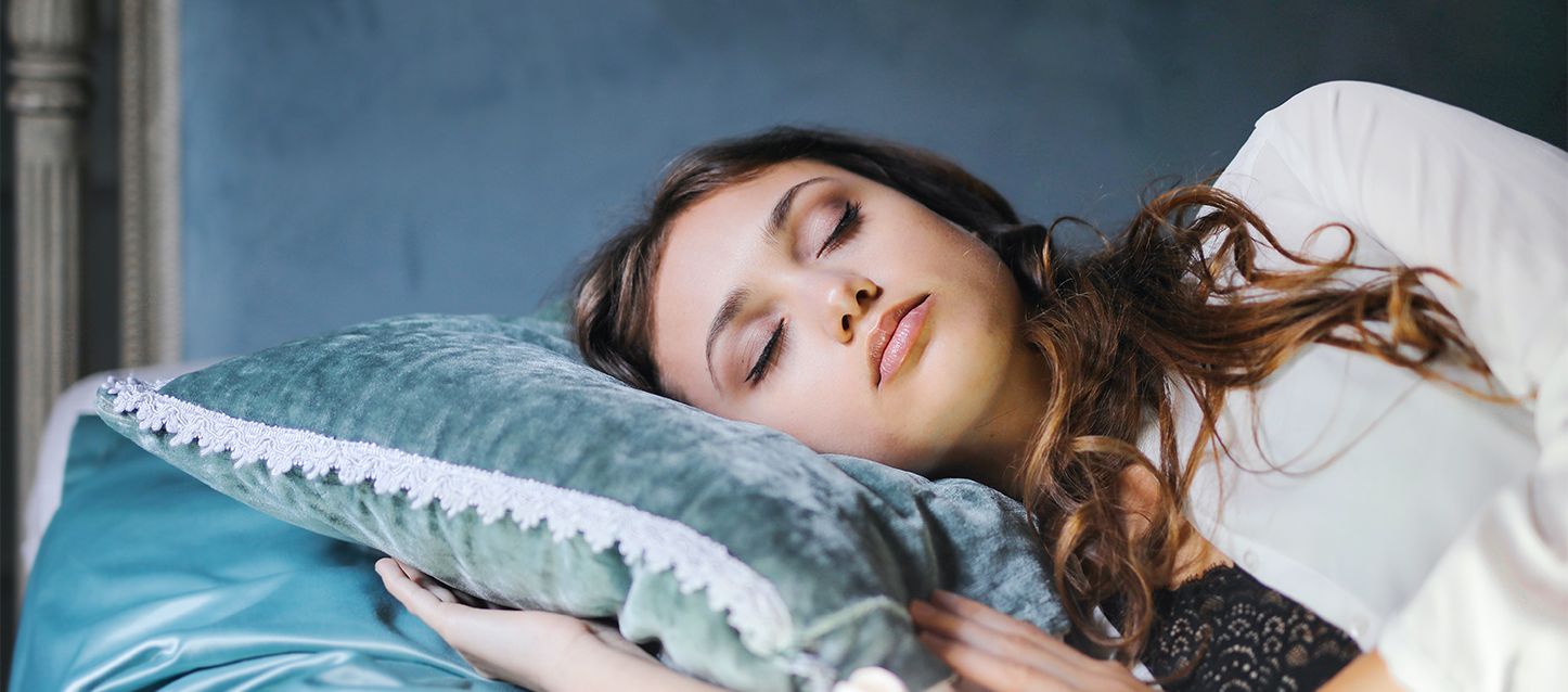 chica de signo sagitario de pelo castaño durmiendo de lado con pijama blanco y apoyandose en cojines de color aguamarina