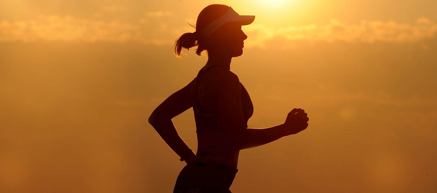 chica con outfit de running con visera blanca corriendo al atardecer