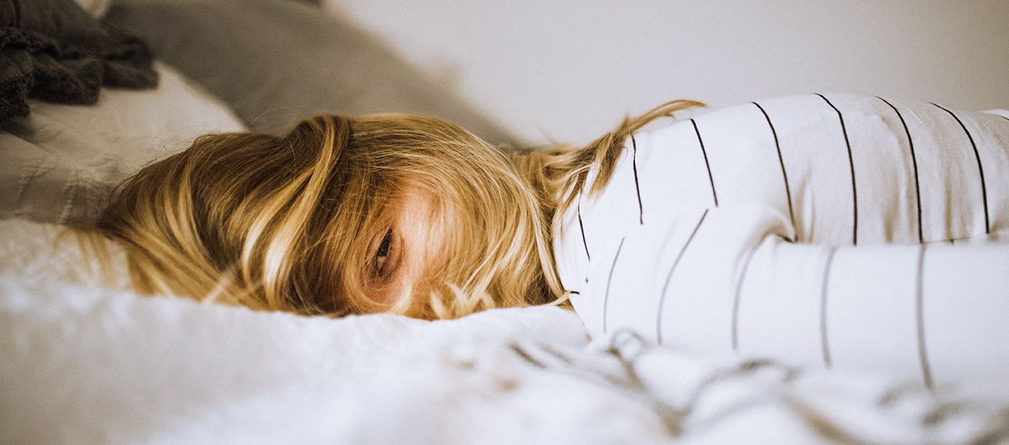 chica rubia con el pelo por la cara tumbada boca abajo en la cama mirando de lado con camiseta blanca y rayas negras