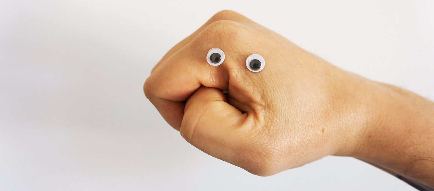 puño cerrado de una persona con dos ojos y haciendo la forma de una boca con el dedo pulgar