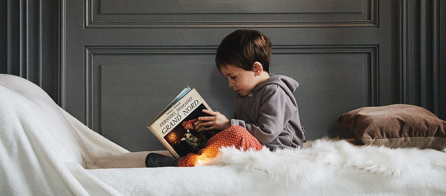 niño pequeño sentado en una cama leyendo un libro
