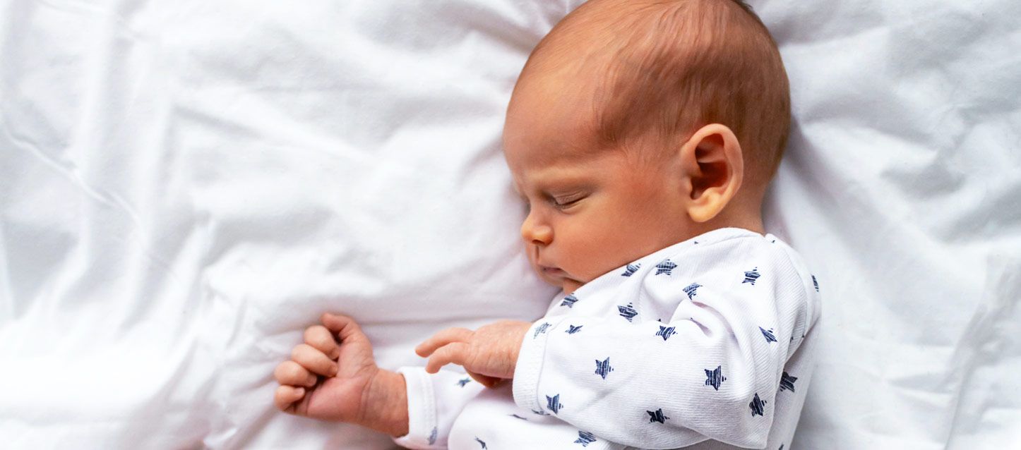 bebe durmiendo con pijama blanco con estrellas azules en una cama