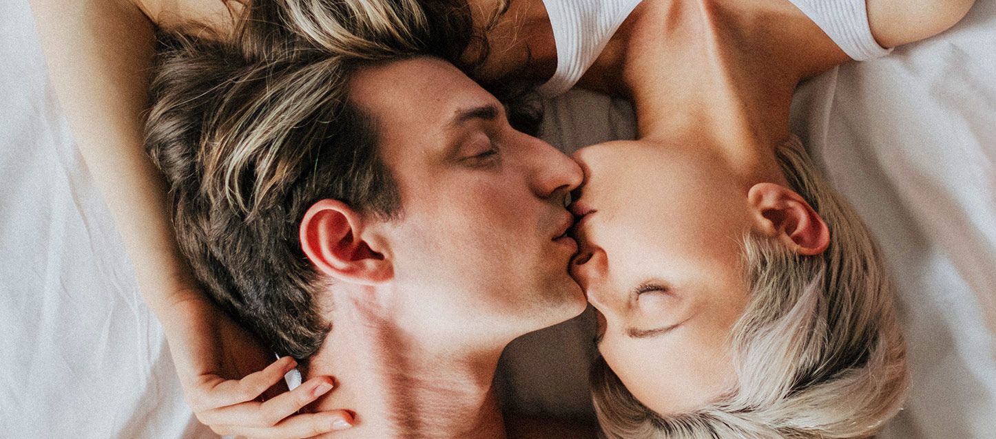 pareja en la cama con las cabezas en dirección opuesta juntado sus labios