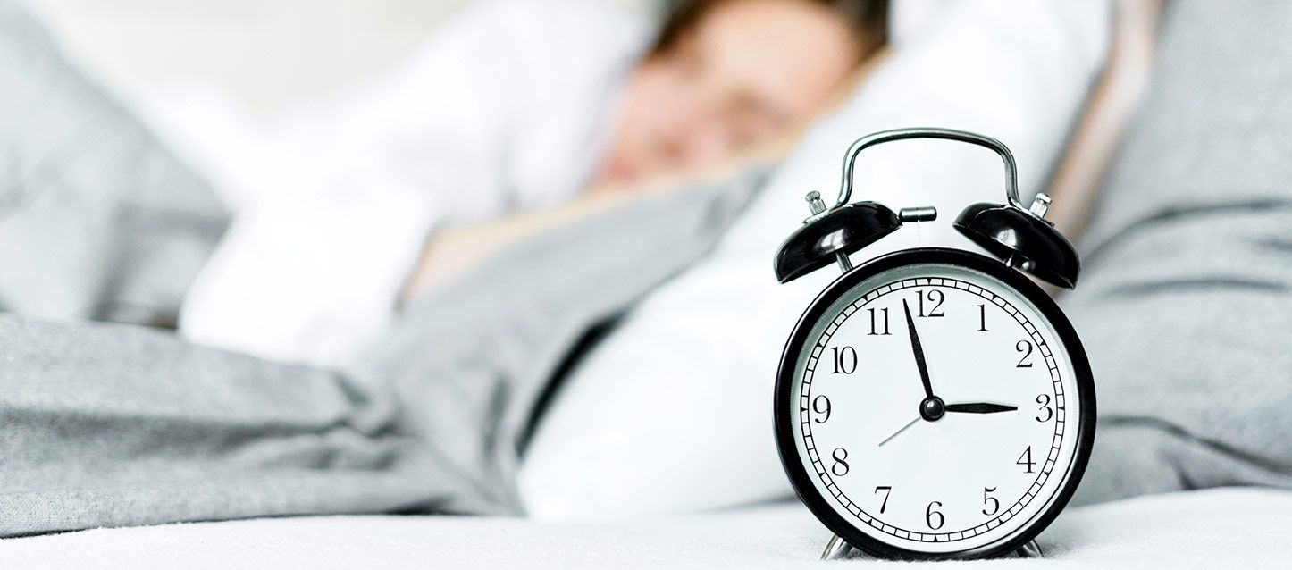 persona durmiendo en la cama y un despertador negro y blanco que marca casi las 3 de la mañana