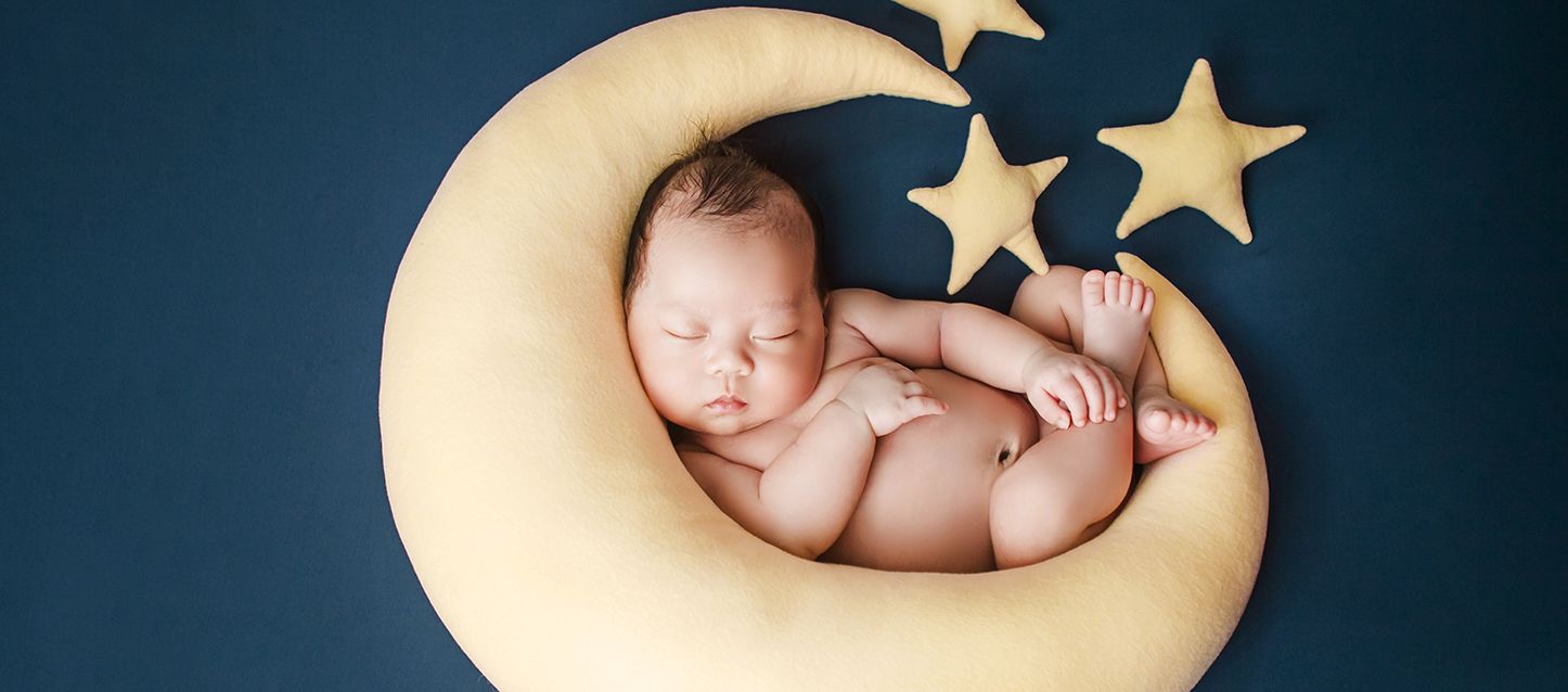 bebe dormido dentro de un cojin con forma de luna y estrellas