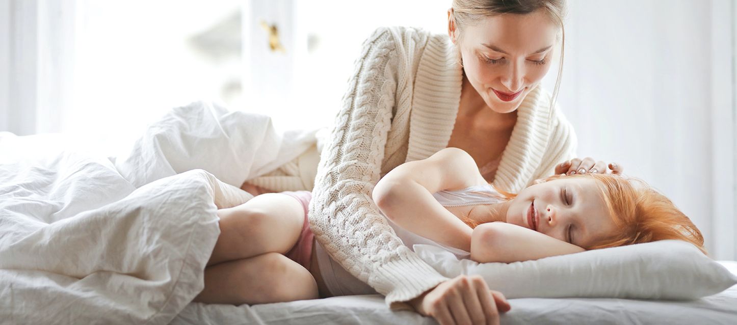 niña pelirroja echando la siesta en la cama mientras su madre le toca el pelo