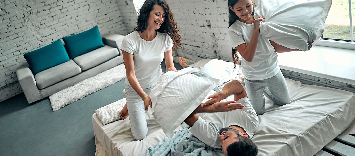 1 chico y dos chicas vestidos con pijama blanco haciendo guerra de cojines