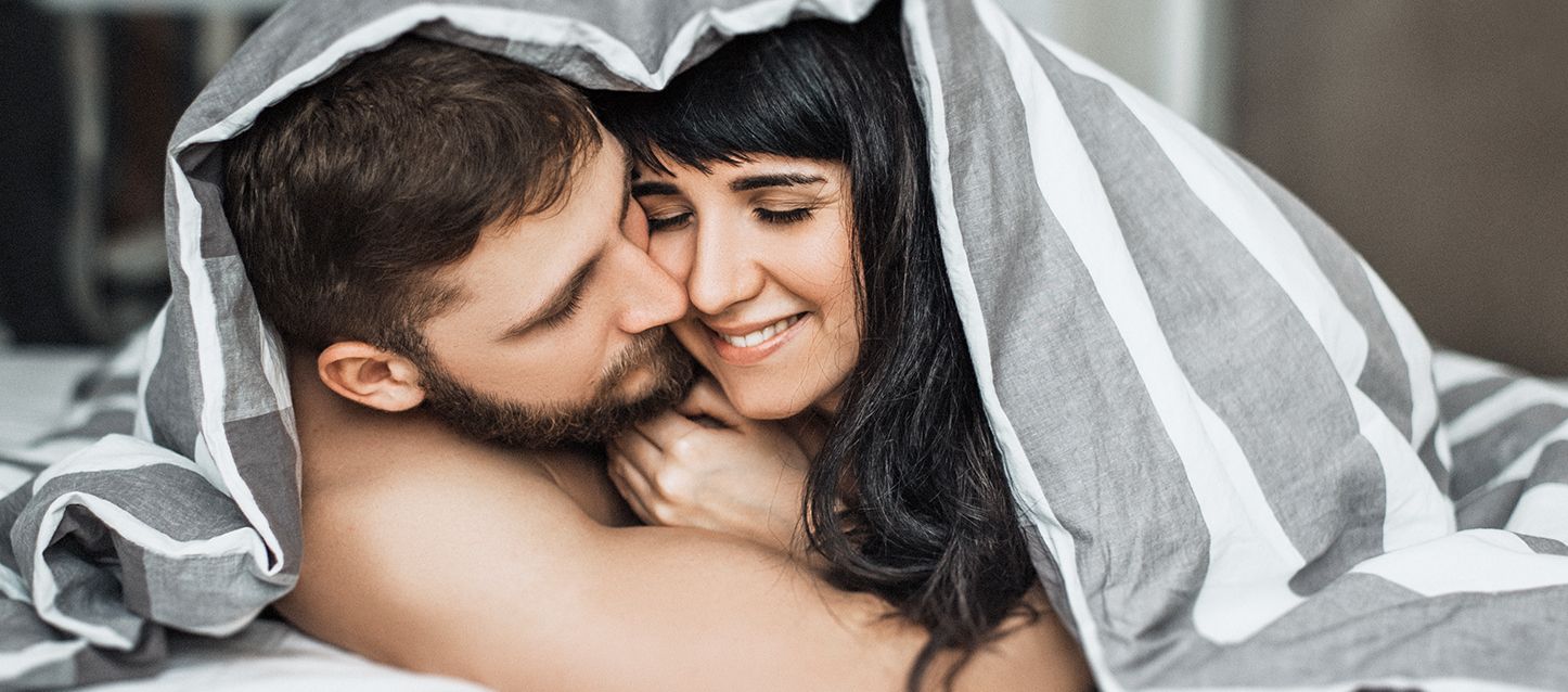 pareja dentro de la cama tapados con la sabana hasta la cabeza sonrientes y abrazados