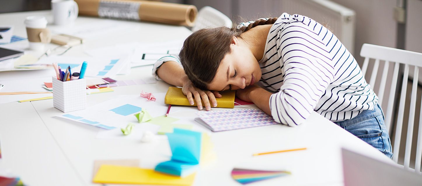 mujer dormida sobre el escritorio sobre su agenda con la mesa con utensilios de diseño