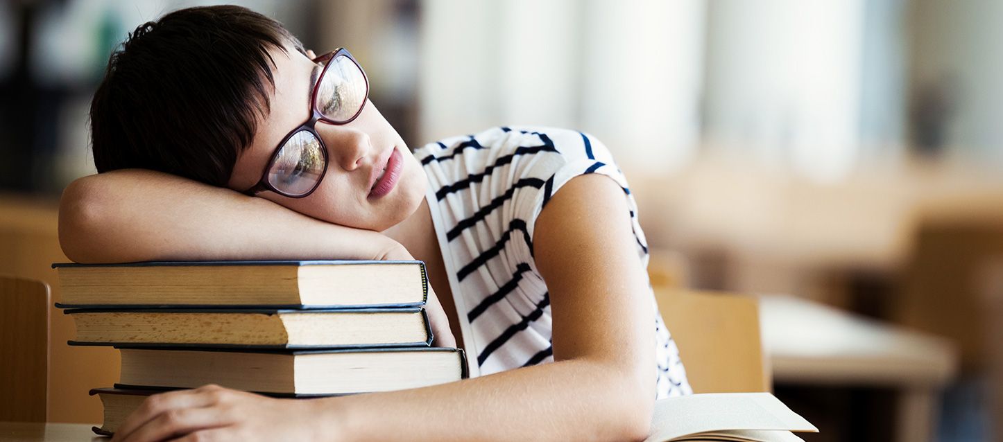 chica morena de pelo corto y gafas con camiseta blanca y rayas negras dormida apoyada sobre un monton de libros