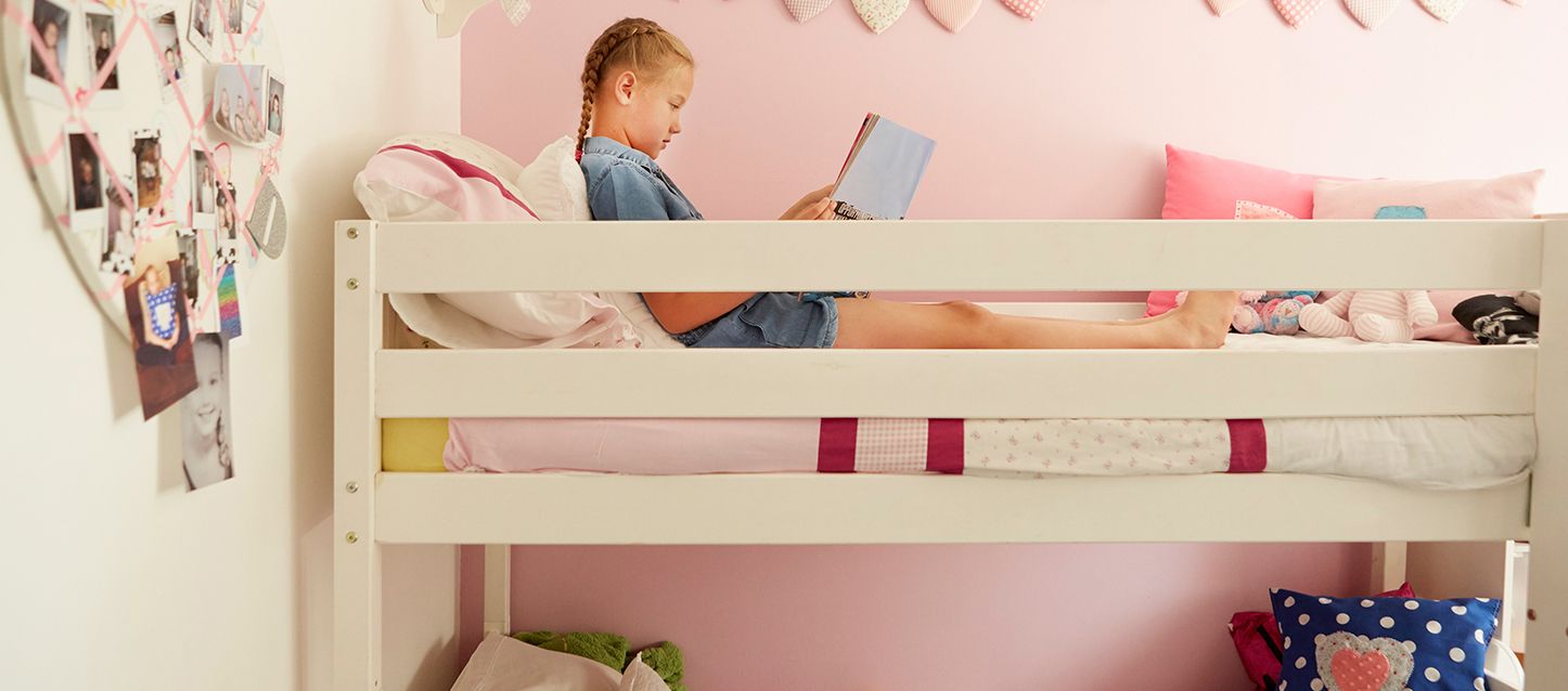 niña de coletas rubias leyendo en la cama de arriba de una litera