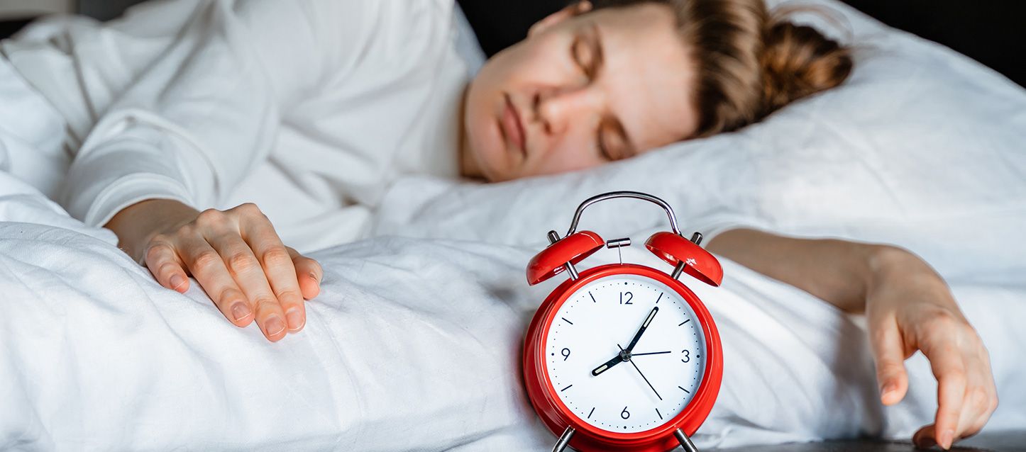 mujer con pijama blanco durmiendo y un despertado rojo