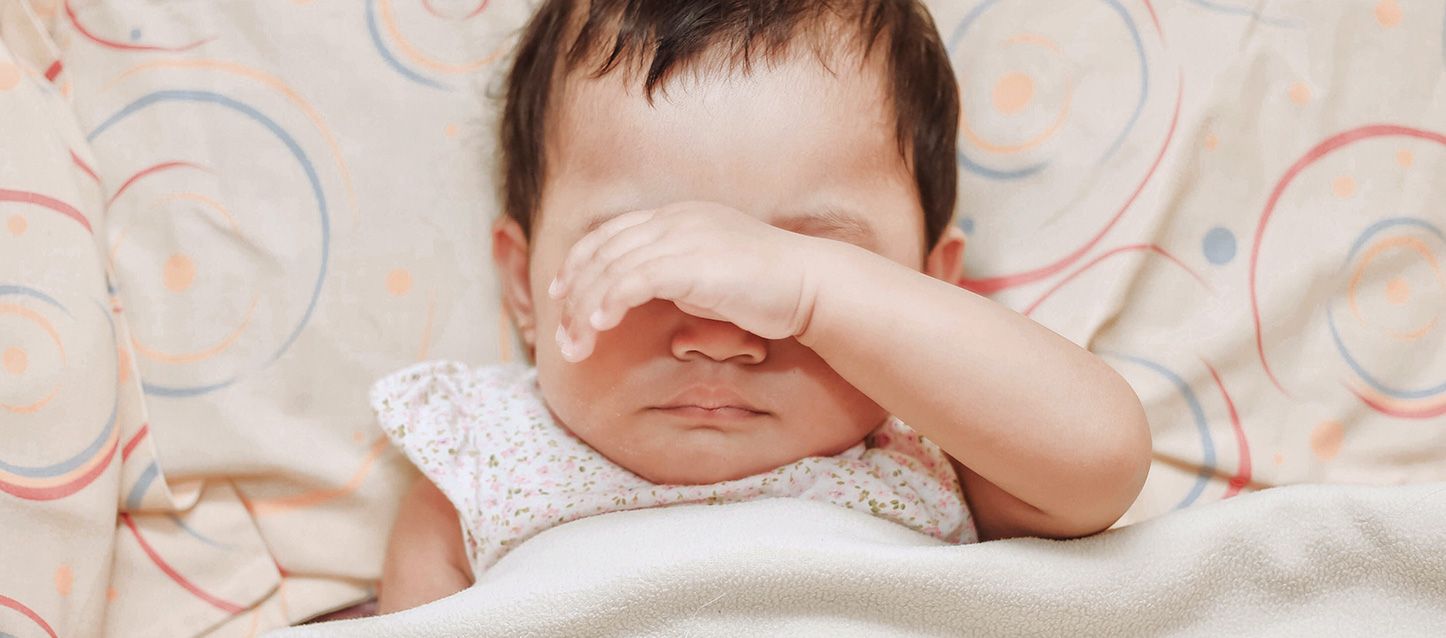 bebe durmiendo boca arriba con la mano sobre sus ojos
