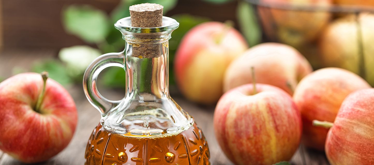 tomar vinagre de manzana antes de dormir y una botella de vinagre sobre una mesa junto a varias manzanas rojas