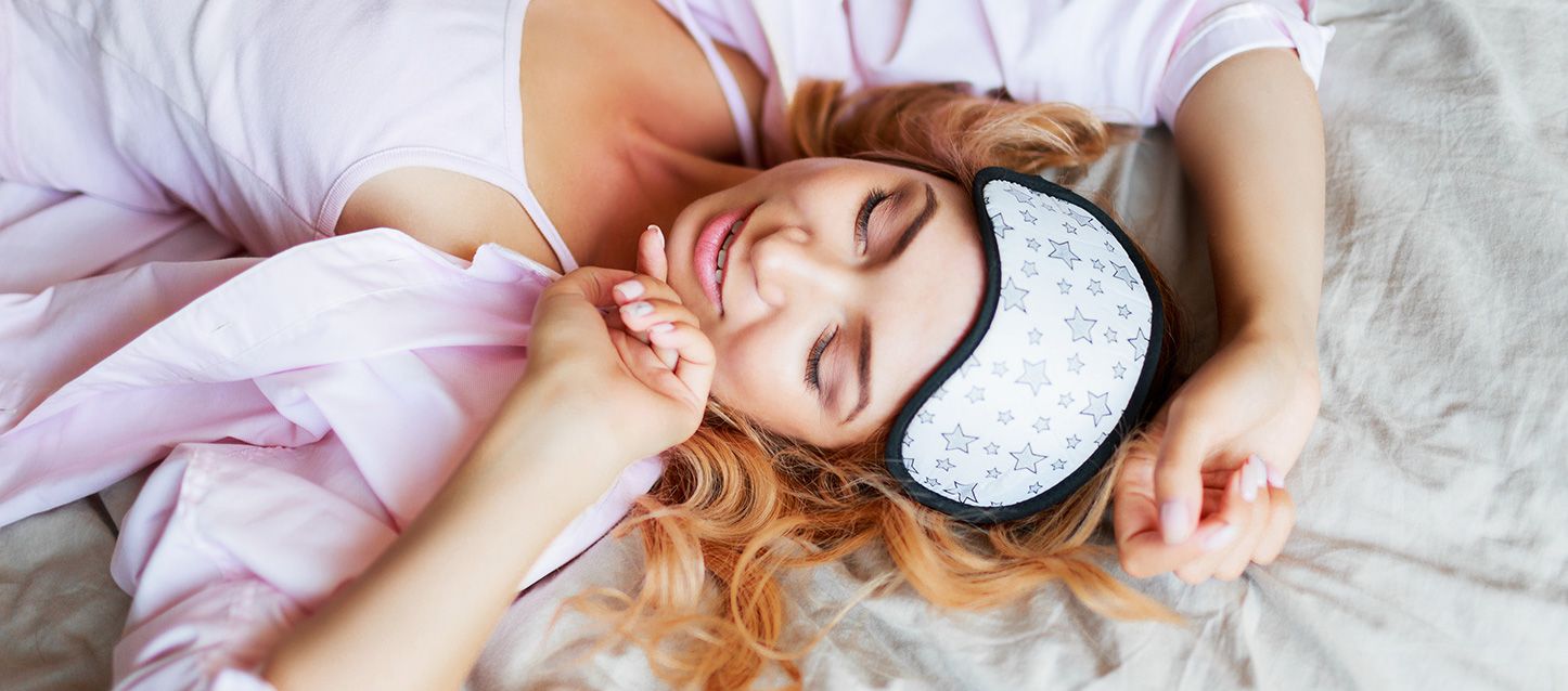mujer de pelo castaño claro despertando en su cama con antifaz en la frente metida