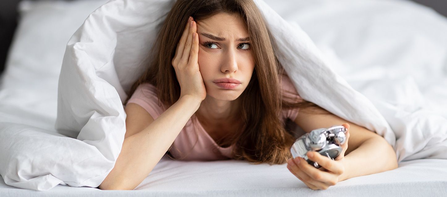 chica con problemas de sueño con dysania metida en la cama con cara de malestar