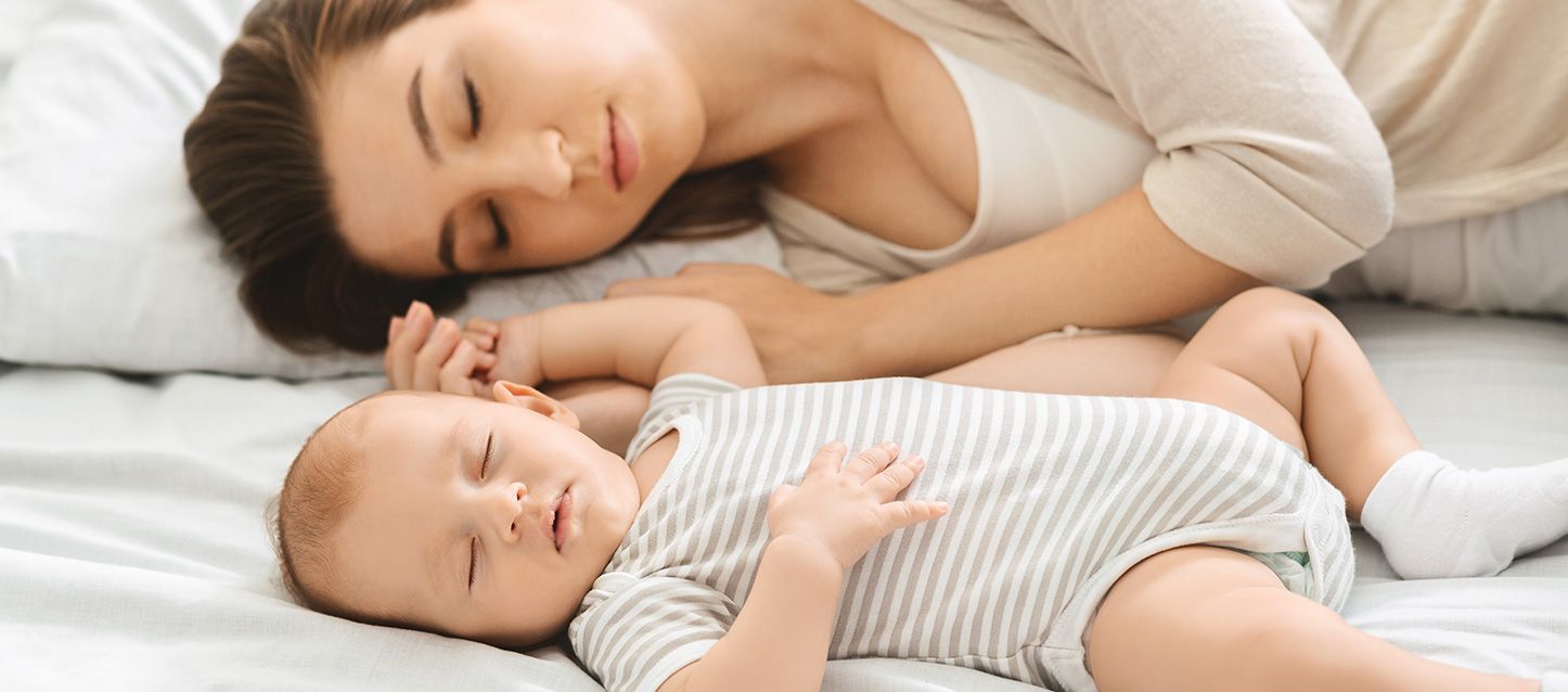 madre durmiendo junto a su bebé en la cama