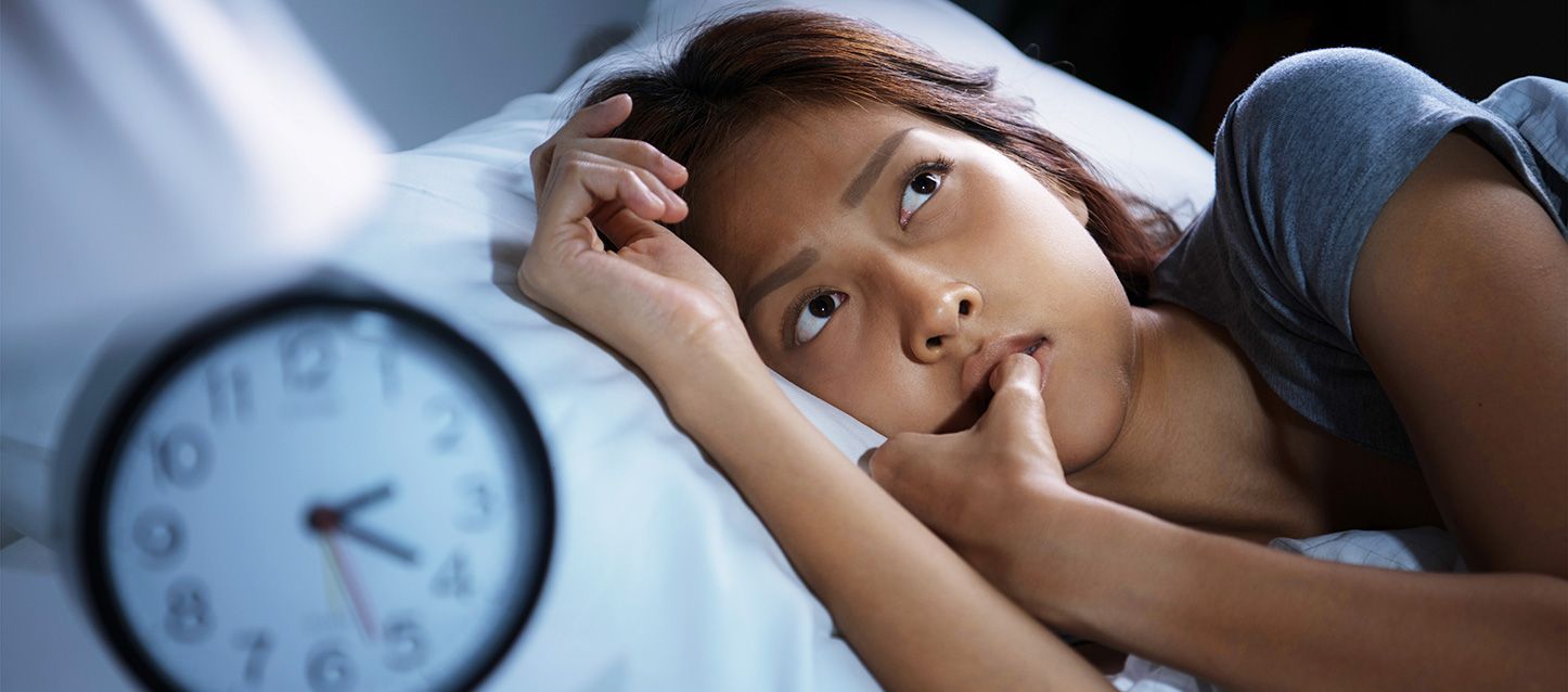 chica metida en la cama sin poder dormir mirando hacia arriba con gesto preocupado