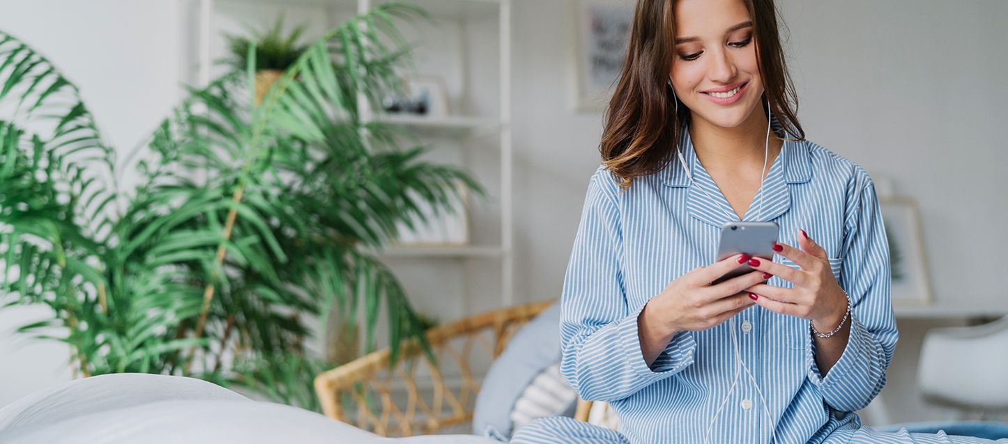 Chica de pelo largo moreno y pijama a rayas azules y blancas usando las mejores apps para controlar el descanso