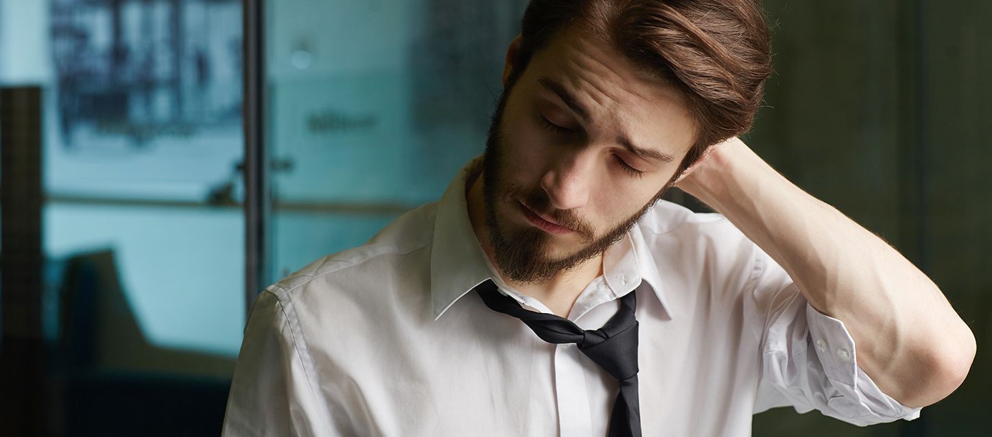 hombre con barba vestido con camisa blanca y corbata negra con la mano en la cabeza y gesto dolorido