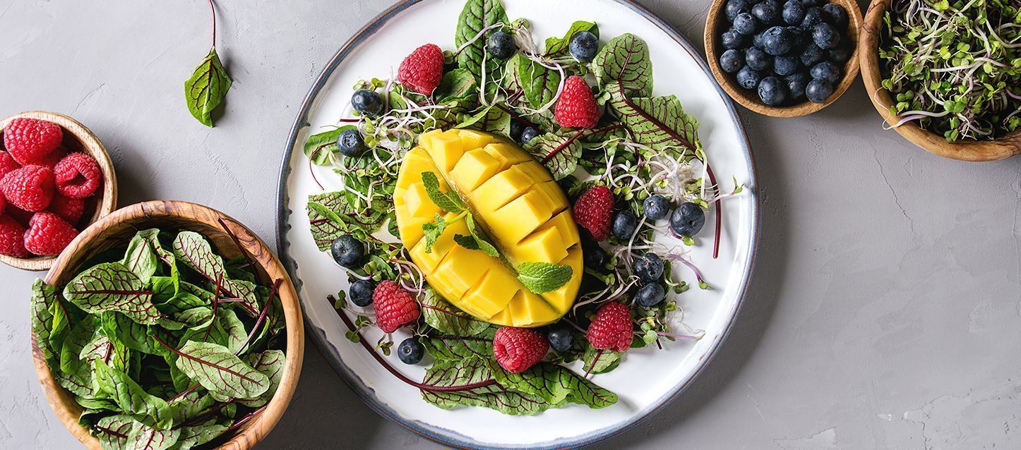 plato con hojas verdes de ensalada, bayas, frambuesas, germinado y mango