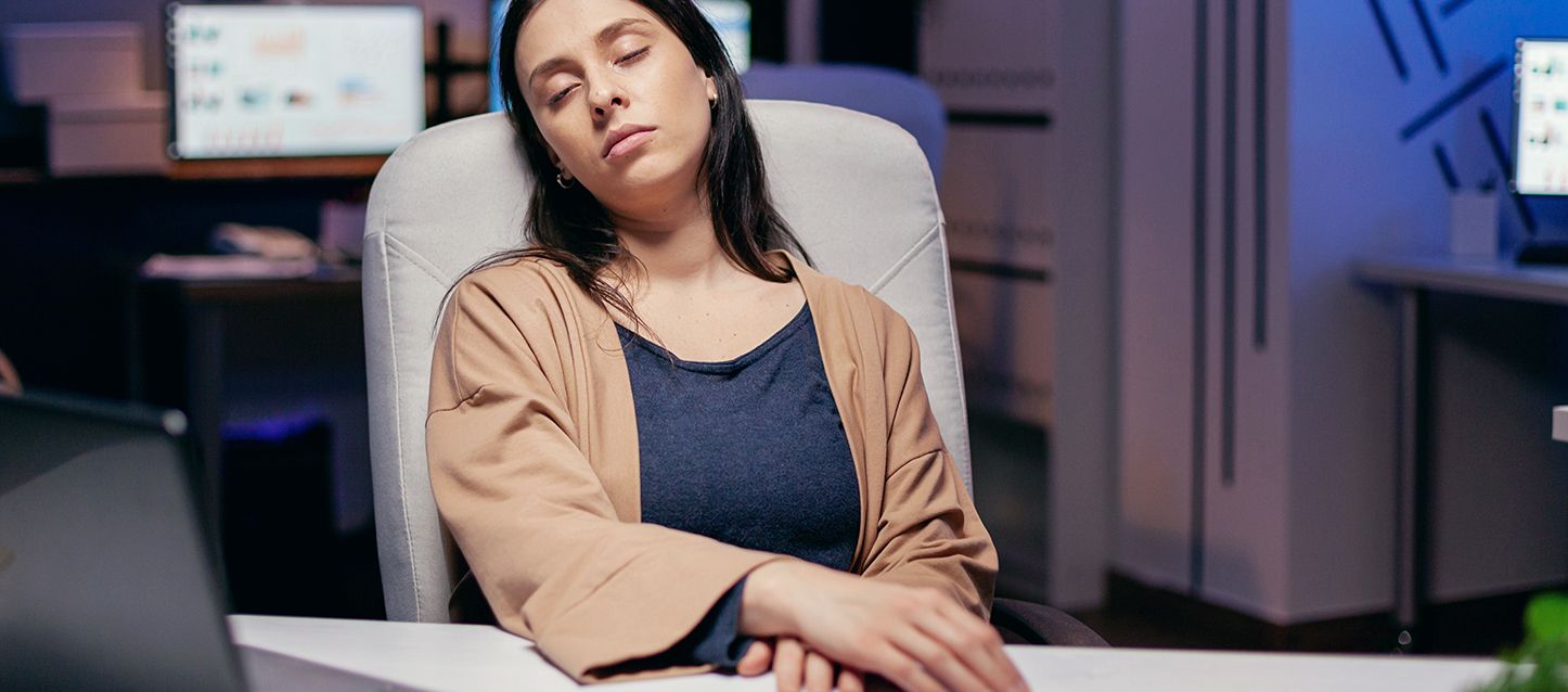 mujer de pelo largo moreno con chaquetilla marron y camiseta azul marino dormido en una silla en una habitación