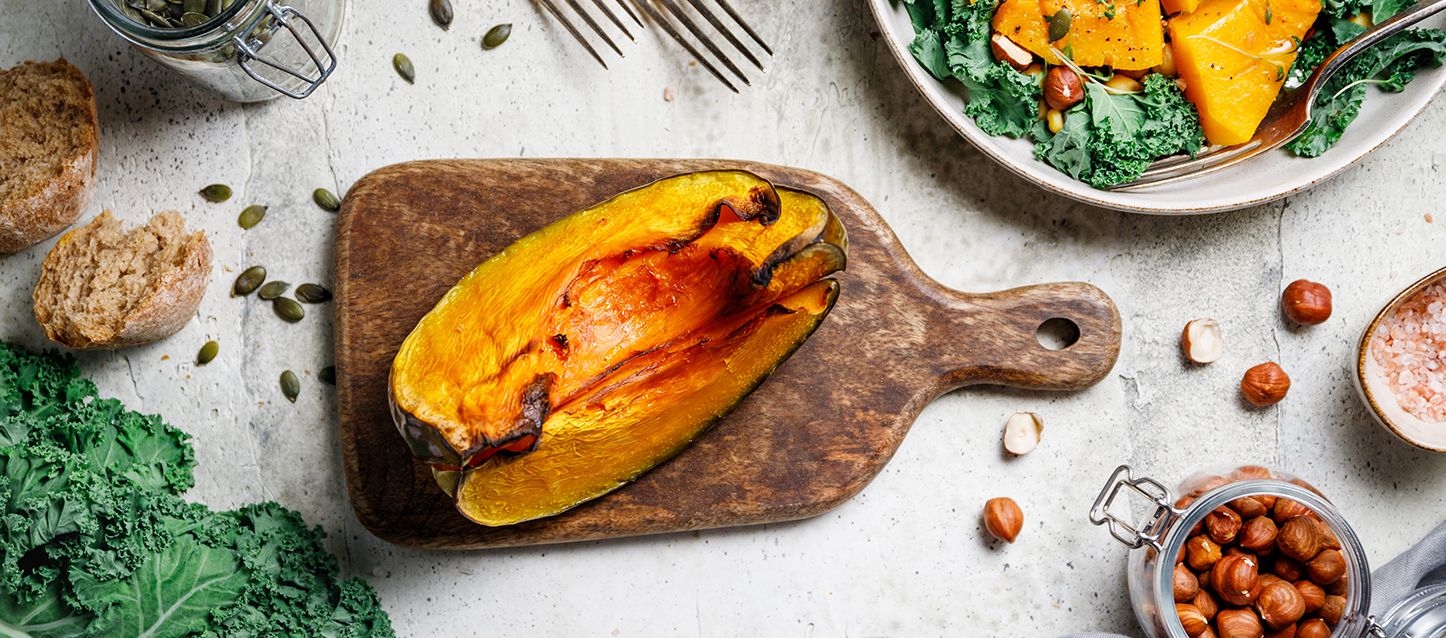 trozo de calabaza al horno sobre una tabla de madera en una mesa con frutos secos y vegetales