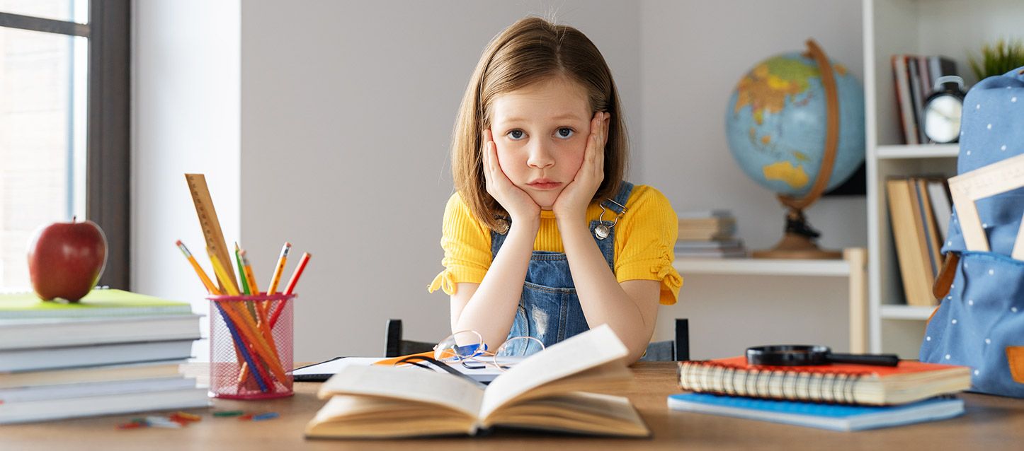 niña pequeña con sueter amarillo y mono vaquero con las manos en la cara con cara de estresada enfrente de un libro