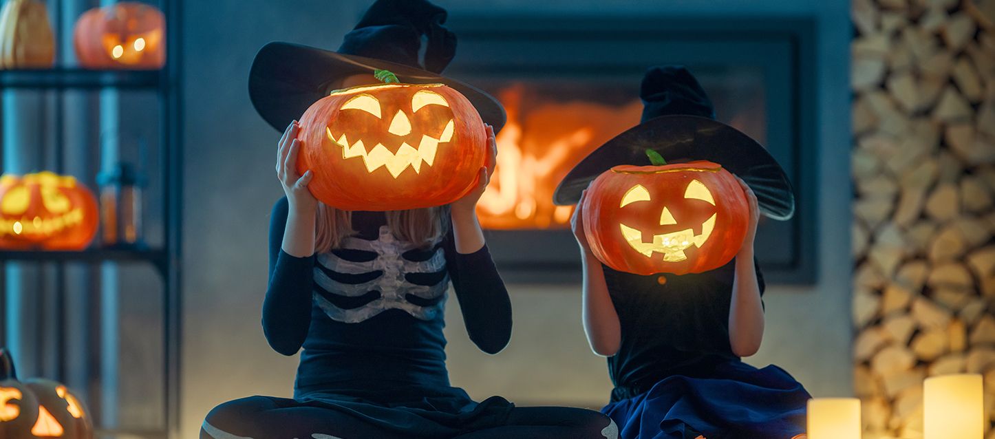 2 niños disfrados de Halloween sujetando cada uno una calabaza de Halloween a la altura de su cabeza