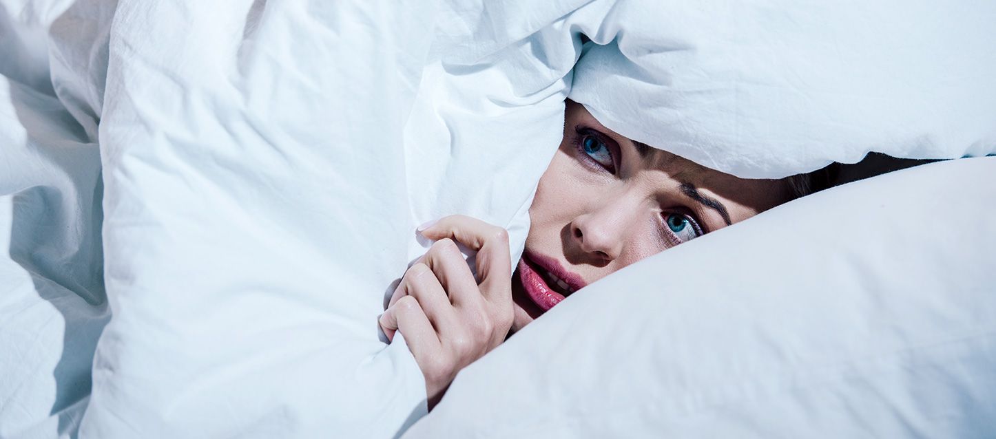 chica de ojos azules tapada con el edredon hasta la cara con cara de miedo por soñar con sangre