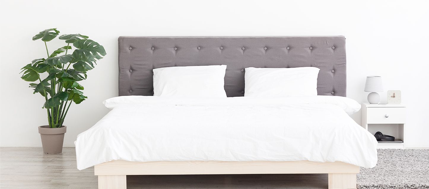 Habitación estilo nórdico con soporte, cama, cabecero color gris, mesita de noche y al otro lado una planta
