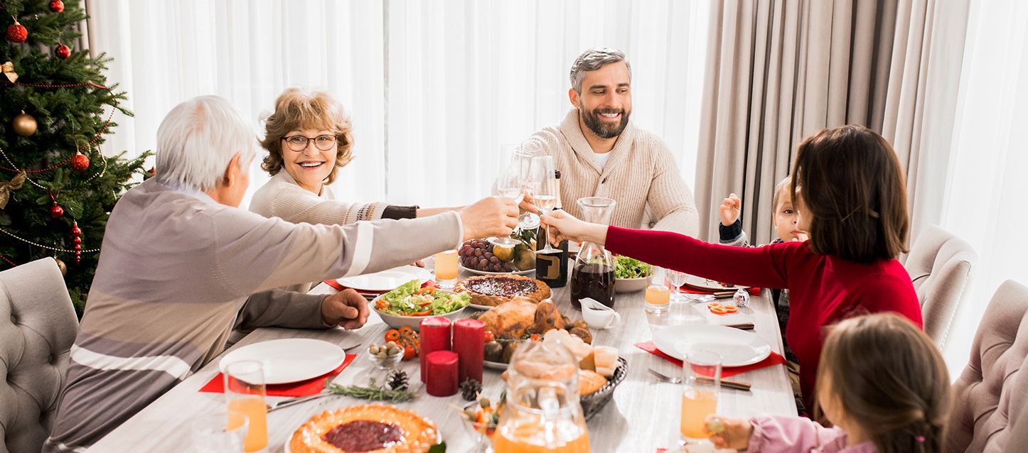 Familia compuesta por dos abuelos y dos padres sentada en la mesa comiendo con dos hijos pequeños