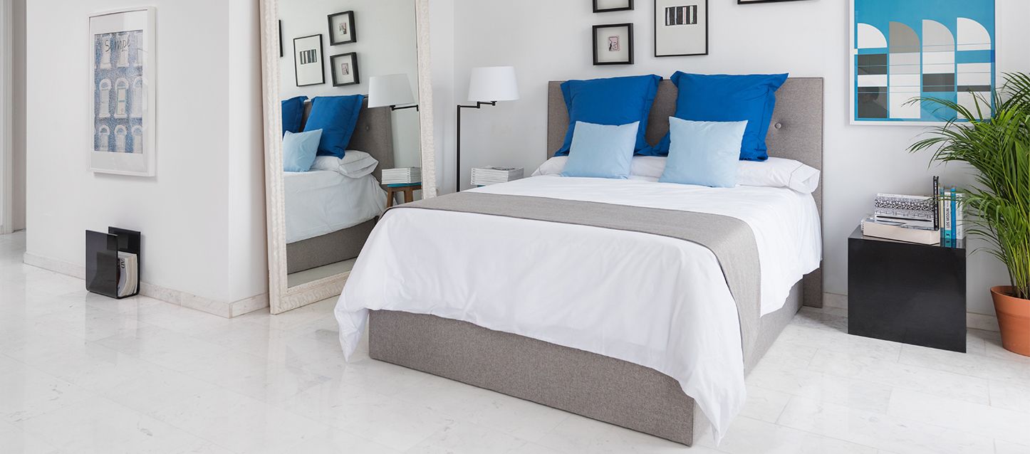 Habitación con una cama, almohada y cojines, mesita de noche con libros y espejo a la derecha y espejo en la parte izquierda
