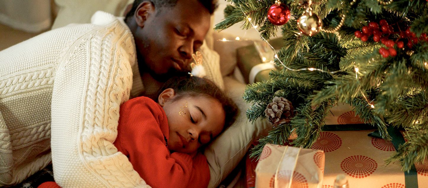 Un padre y su hija durmiendo juntos en el sofá junto al árbol de navidad