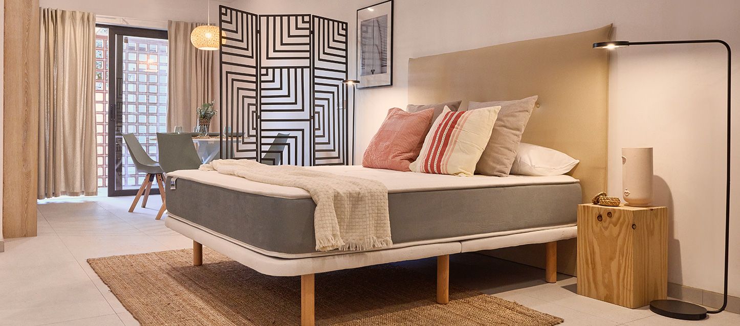 Habitación con base y colchon sobre la que hay varias almohadas y cojines